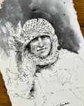 A black and white charcoal or ink sketch of a person wearing a knit hat, rendered on torn white paper with dark smoky washes, photographed on a wooden surface.